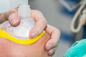 Closeup of an anesthetist at a operating room holding an oxygen mask on patient face photo