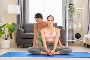 Two beautiful sporty women practice yoga with partner at home. Trainer helps student to do Baddha Konasana exercise or Butterfly pose photo