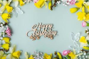 Happy birthday text with spring flowers flat lay frame composition on colored background photo
