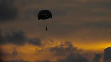 Alone parachute flying against the colorful sunset, sunrise sky above the sea. Extreme sports, parachuting. Summer vacation and holiday video