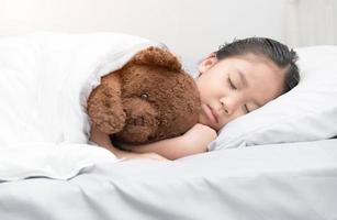 linda pequeño asiático niña dormir y abrazo osito de peluche oso foto