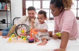 padres con pequeño niña tener divertido jugando con tu nuevo juguetes en el dormitorio juntos. juguetes ese mejorar para niños pensando habilidades. foto