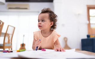 A little child's imagination is represented through colored pencil drawings, with the mother attentively supervising in the living room of the house. photo