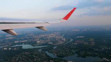 Airplane over the city, porthole. View of the wing from the window of the aircraft. Passenger plane descending for landing, POV video