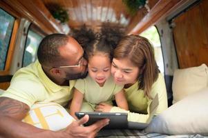 el espalda de un blanco clásico camioneta, pequeño niños jugar y aprender acerca de el mundo en su tableta con padres tomando cuidado de Ayudar. foto