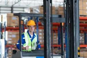 Worker in auto parts warehouse use a forklift to work to bring the box of auto parts into the storage shelf of the warehouse waiting for delivery to the car assembly line photo