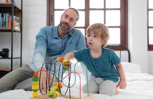 padre con pequeño chico tener divertido jugando con tu nuevo juguetes en el dormitorio juntos. juguetes ese mejorar para niños pensando habilidades. foto