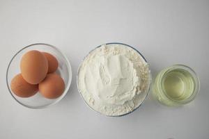 trigo harina en un bol, huevos y petróleo en mesa foto