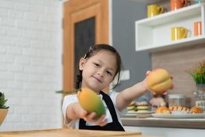 retrato de un pequeño niña en el cocina de un casa teniendo divertido jugando con Fruta juguete y batería de cocina foto