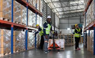 trabajador en auto partes almacén utilizar un carretón a trabajo a traer el caja de auto partes dentro el almacenamiento estante de el almacén esperando para entrega a el coche montaje línea foto