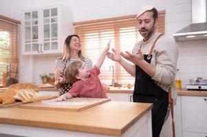 Mom and dad in the kitchen of the house with their small children. Have a good time baking bread and making dinner together. photo