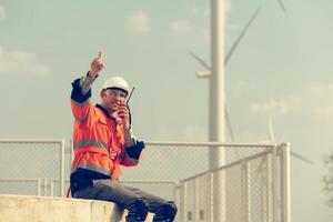 ingeniero a natural energía viento turbina sitio con un misión a tomar cuidado de grande viento turbinas utilizar un walkie película sonora a comunicar con un colega trabajando en parte superior de el viento turbina. foto