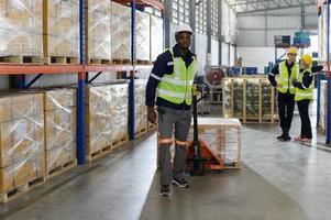 trabajador en auto partes almacén utilizar un carretón a trabajo a traer el caja de auto partes dentro el almacenamiento estante de el almacén esperando para entrega a el coche montaje línea foto