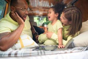 The back of a white classic van, little kids play and learn about the world on their tablet with parents taking care of helping. photo