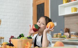 Portrait of a little girl in the kitchen of a house having fun playing with fruit toy and kitchenware photo