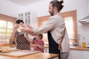 Mom and dad in the kitchen of the house with their small children. Have a good time baking bread and making dinner together. photo