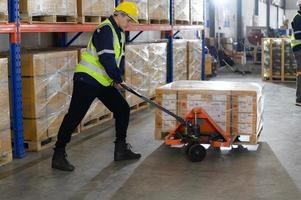 trabajador en auto partes almacén utilizar un carretón a trabajo a traer el caja de auto partes dentro el almacenamiento estante de el almacén esperando para entrega a el coche montaje línea foto