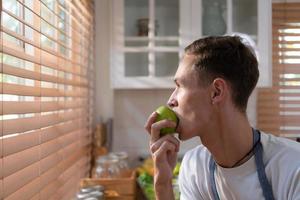 joven lgbt entra el cocina a hacer un Fruta y vegetal ensalada para cena. comiendo manzana mientras esperando para el Pareja a ven hogar. foto