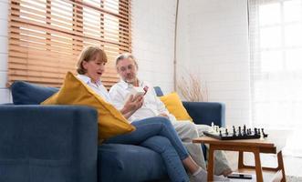 Old couple Sit and relax in the living room of the house. Along with the surprise from the husband who prepared a wedding anniversary gift. photo