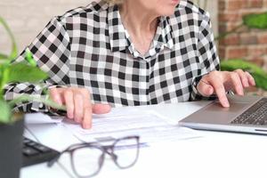 Close-up of a woman's hands with a utility bill, and a calculator and a laptop on the table. A woman submits meter readings and fills out invoices for payment for gas, electricity, and heating costs. photo