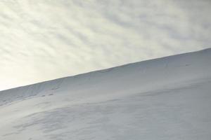 Snowy slope against sky. Avalanche of snow on mountain ridge. Winter weather. photo