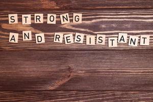 Strong and resistant phrase, lettering on wooden background photo