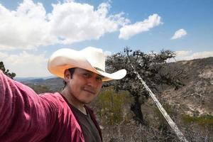 hombre en un vaquero sombrero toma un selfie en frente de un montaña. foto