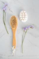 Full body dry massage brush and handmade honey soap from above on marble background with purple flowers photo