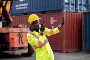 Worker man in protective safety jumpsuit uniform with yellow hardhat and use  Walkie Talkie check container at cargo shipping warehouse. transportation import,export logistic industrial service photo