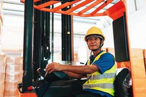 Worker driver asian man in protective safety jumpsuit uniform with yellow hardhat at warehouse forklift loader works photo