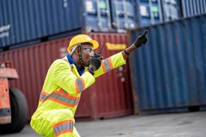 Worker man in protective safety jumpsuit uniform with yellow hardhat and use  Walkie Talkie check container at cargo shipping warehouse. transportation import,export logistic industrial service photo