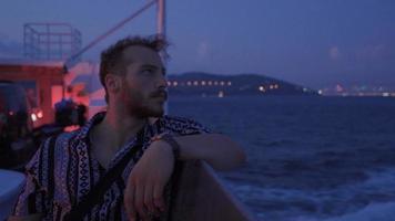 joven hombre mirando a el mar a noche. joven hombre de viaje en el Embarcacion mirando a el mar a noche. video