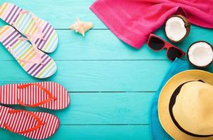 vacaciones de verano divertidas con chanclas, cocos, gafas de sol, toalla y sombrero. accesorios de playa con espacio de copia sobre fondo de madera azul. vista superior. foto