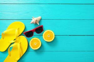 Summer background. Yellow flip flops, red sunglasses, shell and orange fruit on blue wooden background. Top view and summer time. photo