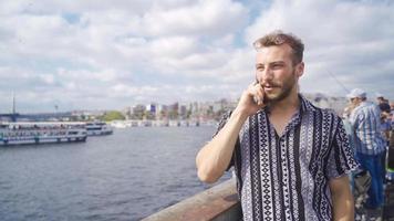 el joven hombre en Estanbul habla en el teléfono. el joven hombre en estambul eminonu cuadrado habla en su teléfono por el mar. video