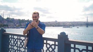 The young man is taking a photo with the phone in Istanbul. Handsome young man by the sea takes pictures and selfies with his phone. video