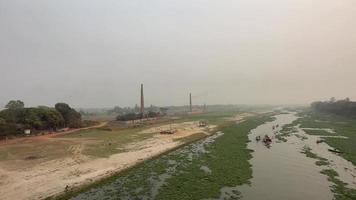 Scenic view of a rural area with a small river and brick kiln on the riverbank. Beautiful nature view with small water vessels on a canal. Kids playing on the Riverbank and boats moving on the river. video