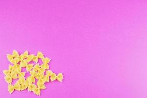 farfalle spread out in the corner on a bright pink background. Pasta pattern. photo