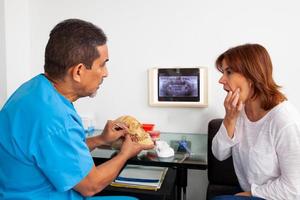 Male middle-aged orthodontic specialist dentist at his office explaining the treatment to his female patient photo