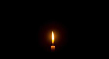 una sola llama de vela encendida o luz que brilla en una vela naranja sobre fondo negro u oscuro en la mesa de la iglesia para Navidad, funeral o servicio conmemorativo con espacio para copiar foto