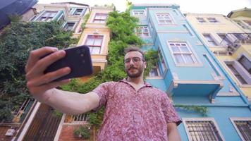 Young man taking selfie with his phone. The young man who wants to take a photo with the colorful houses behind him takes it with his phone. video