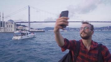 Video call against the bridge and city view on the sea. Istanbul city. Man on the ferry in the Bosphorus is making a video call. In the background are the Istanbul bridge and the ships in the sea.