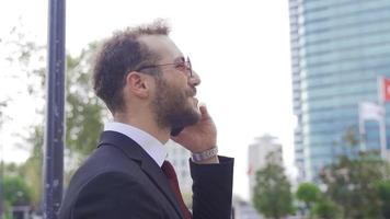 o negócio mobilidade. bonito homem de negocios sorridente enquanto falando em telefone dentro cidade rua. video