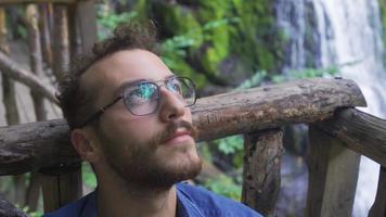 homme à la recherche à le ciel dans la nature. Beau Jeune homme dans des lunettes est content dans le forêt et à la recherche à le ciel. video