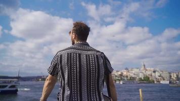 Young Man is looking at the sky against the sea in Istanbul. Handsome young man is stylish and wearing sunglasses and stands against the sea. video