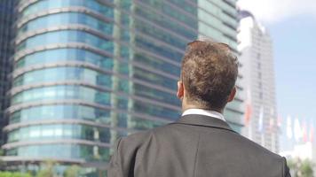 Businessman near high-rise buildings. The businessman looks at his watch and looks at the high-rise buildings around him. video