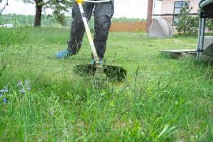 A male gardener mows the green grass of the lawn in the backyard with a gasoline mower. Trimmer for the care of a garden plot photo