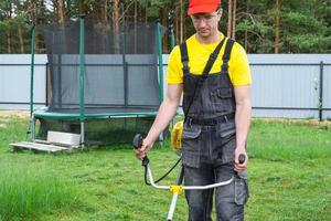 A male gardener mows the green grass of the lawn in the backyard with a gasoline mower. Trimmer for the care of a garden plot photo