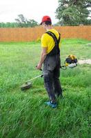 A male gardener mows the green grass of the lawn in the backyard with a gasoline mower. Trimmer for the care of a garden plot photo