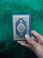 A photo of man hand holding a holy Qur'an with green background for copy space, hand holding a Quran book isolated for copy space